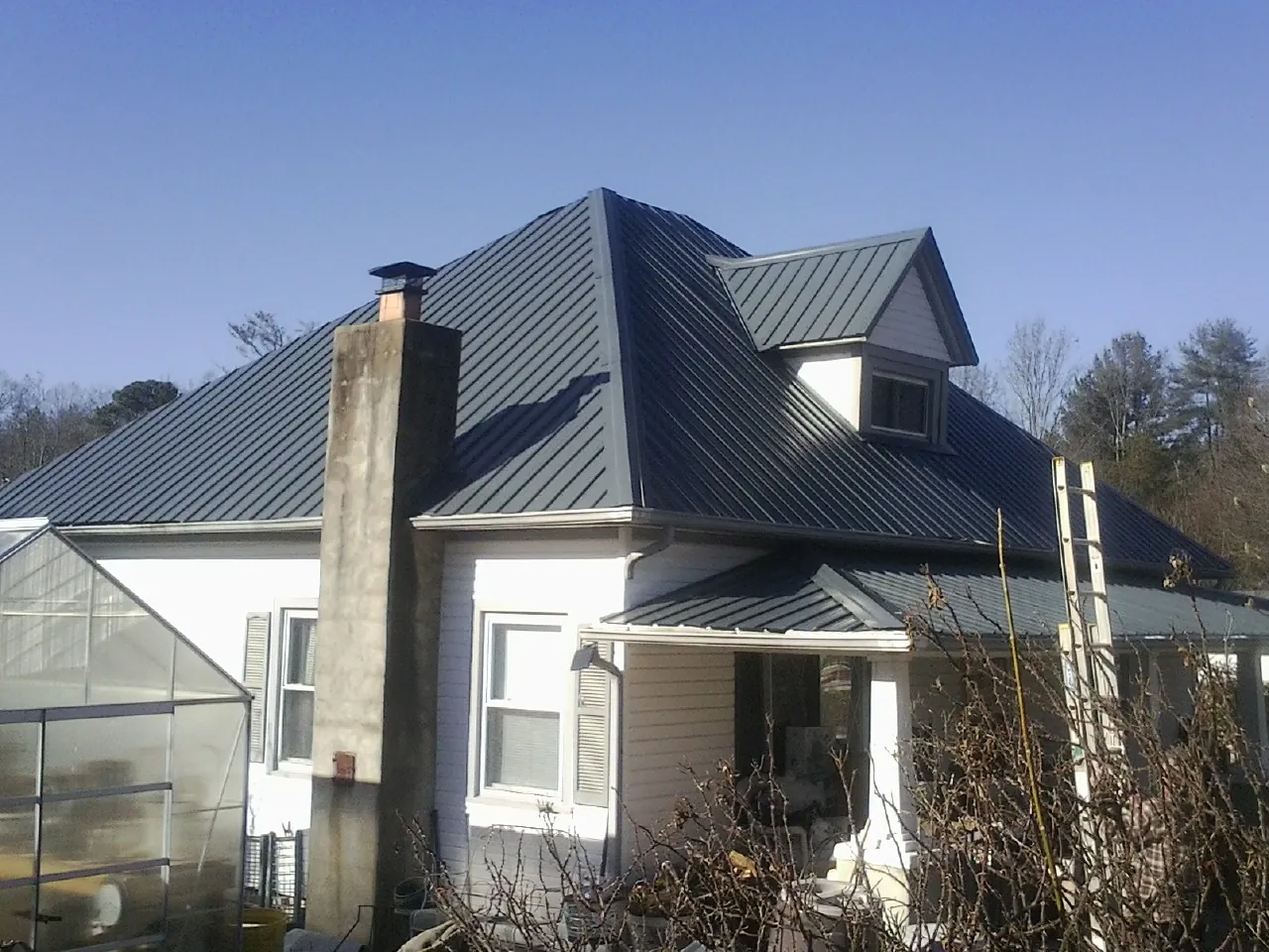 Dark blue standing seam metal roof on a white farmhouse with dormer — Slate & Tile Roof Repair by Roofing Brothers in Erick