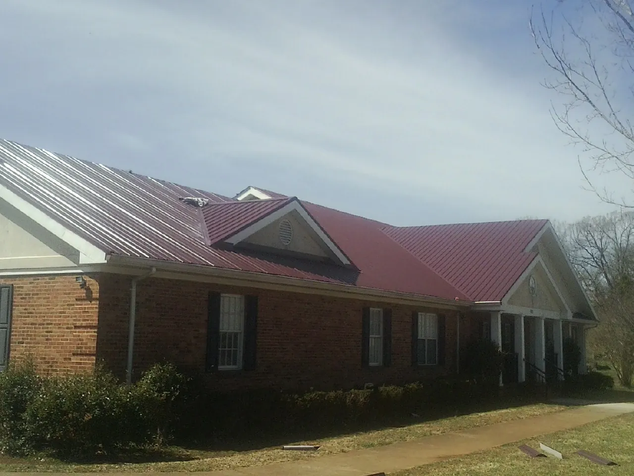 Red metal roof with gabled entries on a long brick building, from a Hail Damage Roof Repair job in Erick
