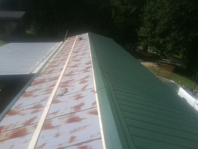 Old rusted panels beside newly installed green metal roofing — Wind Damage Roof Repair by Roofing Brothers in Erick