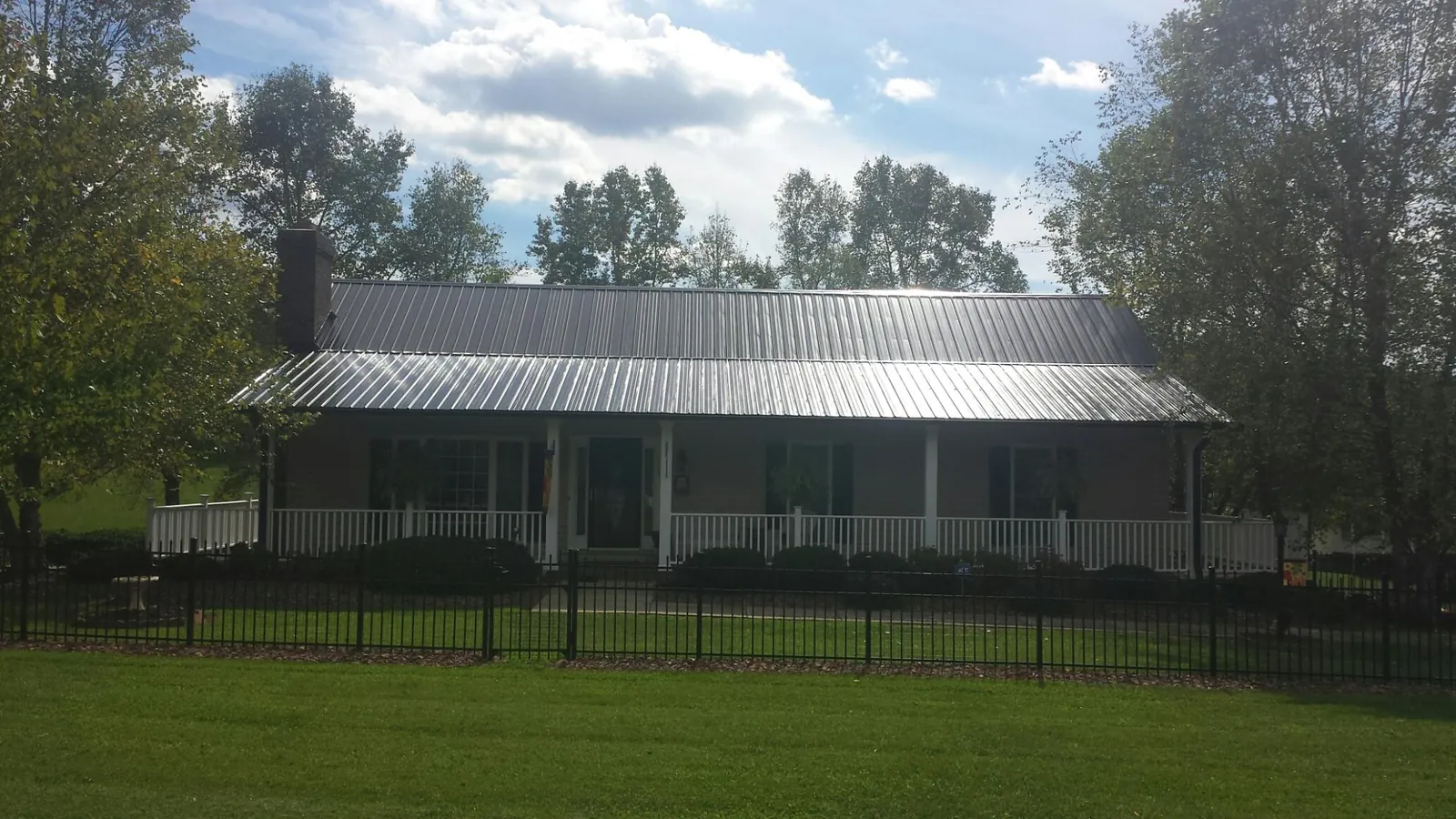 Gray metal roof on a brick ranch with a full width front porch — Gutter Guard Installation work by our crew in Erick