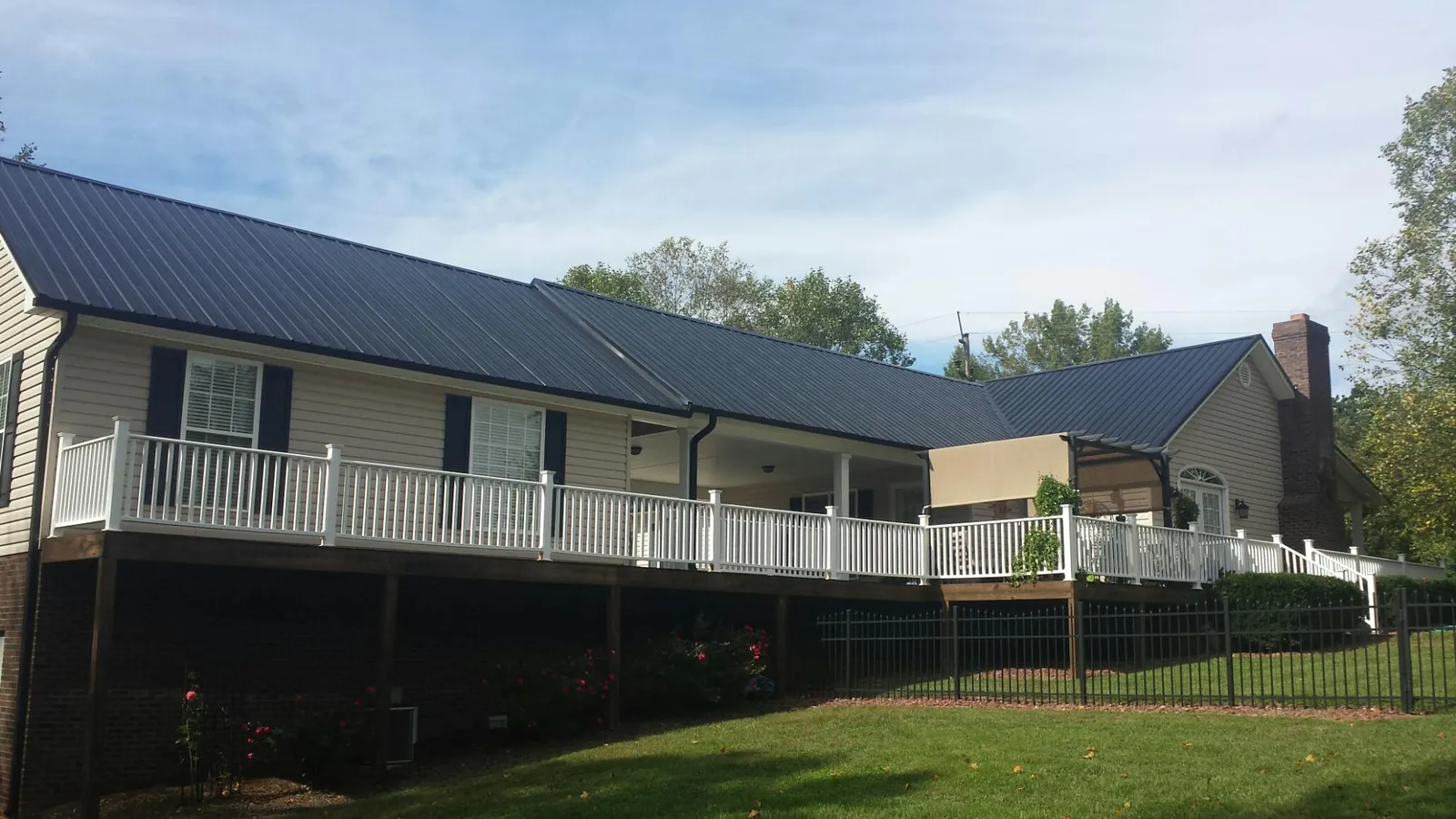 Black metal roof above a long white railed deck on a hillside home in Erick