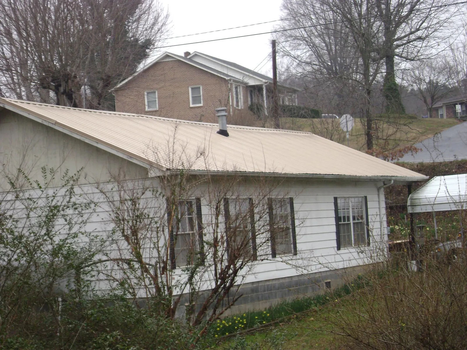 Tan metal roof on a white sided house set into a hillside — Commercial Roofing by Roofing Brothers in Erick