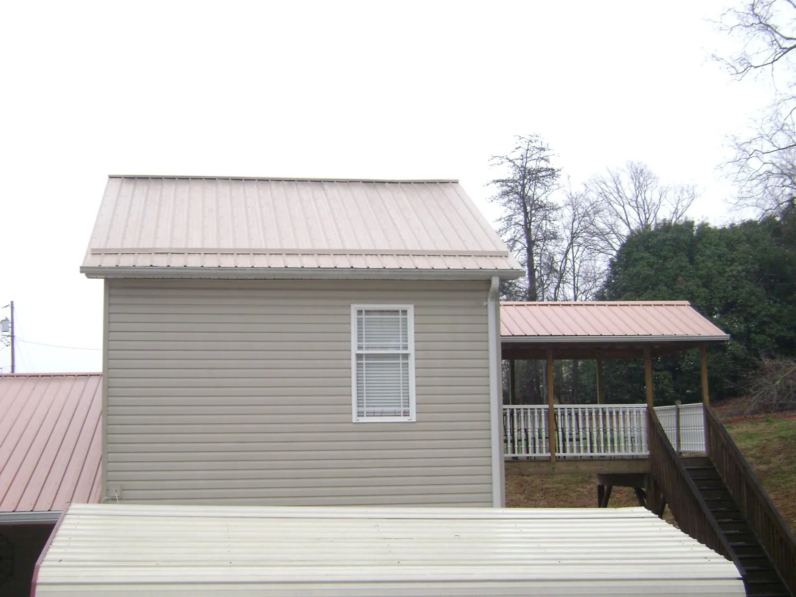 Tan metal roofs on a two story addition and attached porch, from a Roof Replacement job in Erick
